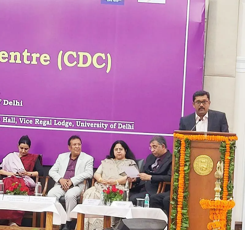 A speaker addressing the Career Development Centre launch from the University of Delhi podium, with the dais seated alongside.