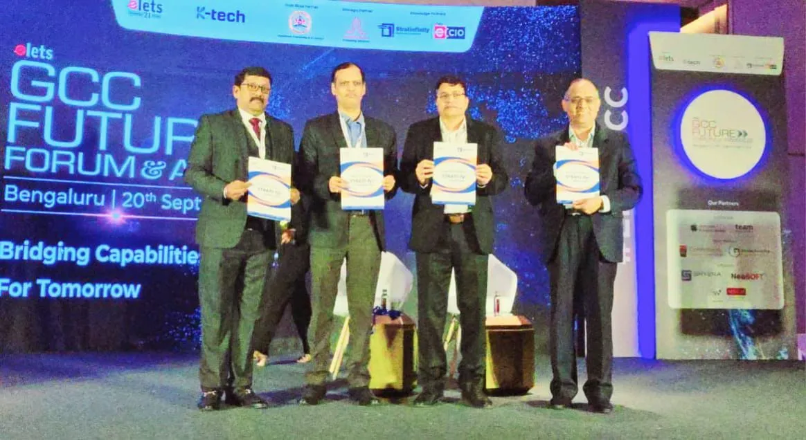 Four delegates on stage holding a StratInfinity publication at the elets GCC Future Forum & Awards in Bengaluru, under the theme 'Bridging Capabilities For Tomorrow'.